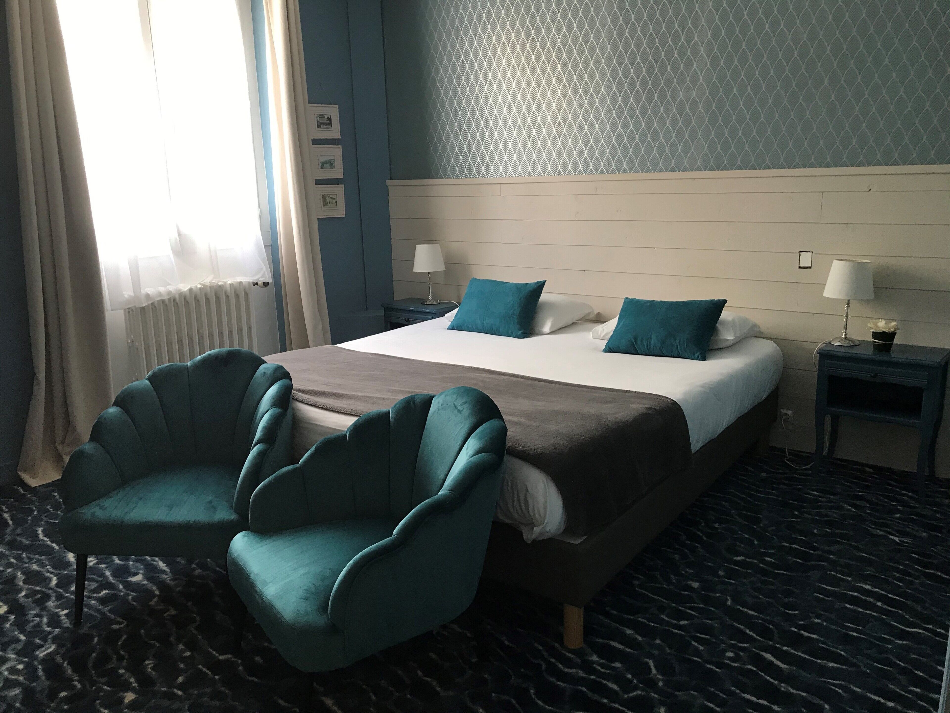 A hotel room with a bed, two chairs, a nightstand, and a lamp.
