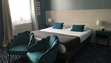 A hotel room with a bed, two chairs, a nightstand, and a lamp.