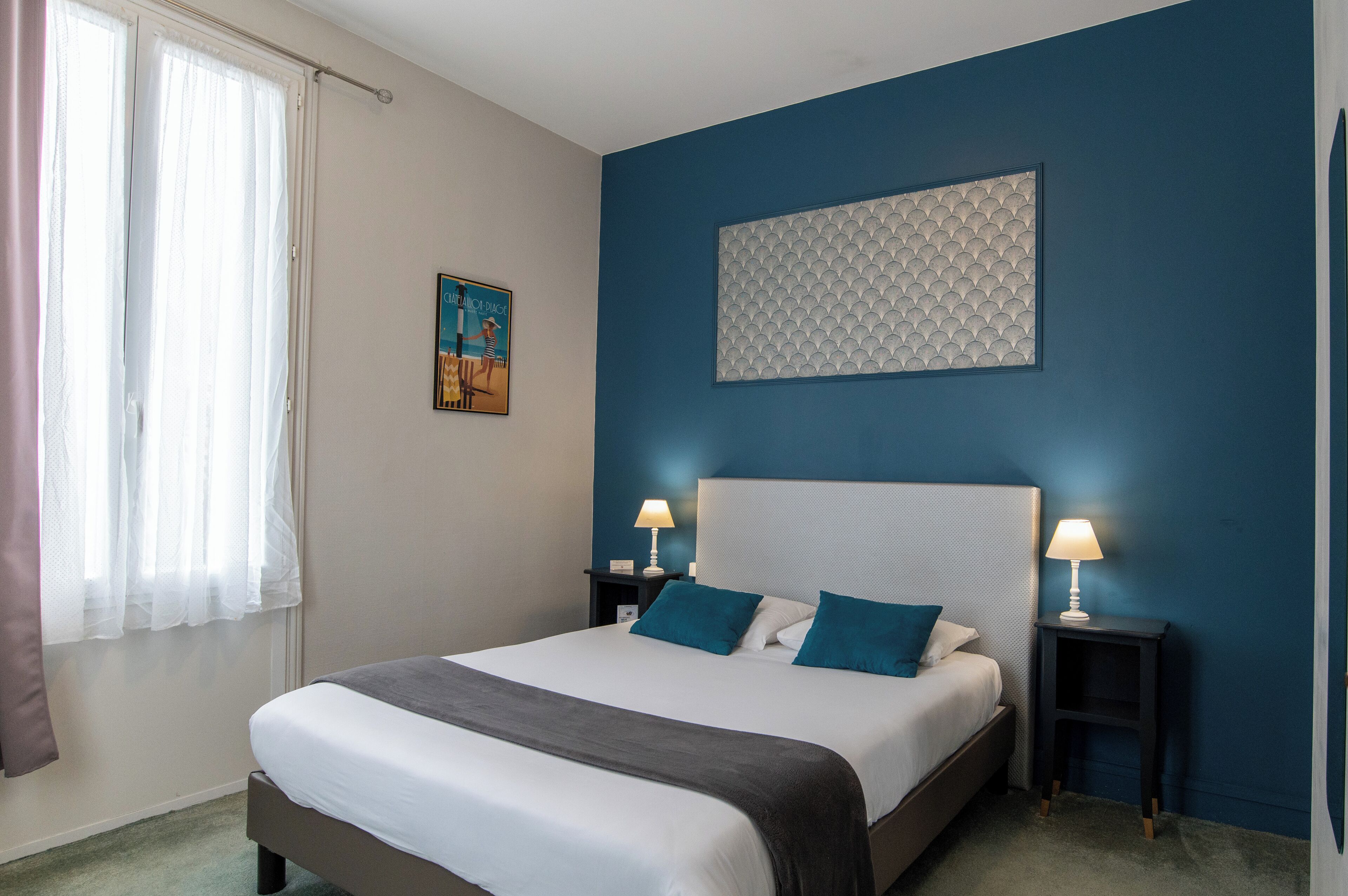 Una cama bien hecha con cabecera, dos mesitas de noche con lámparas, un cuadro en la pared y una ventana con cortinas.
