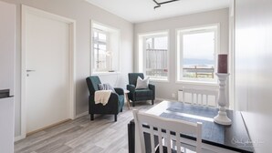Een lichte kamer met twee fauteuils, een eettafel en grote ramen met uitzicht.