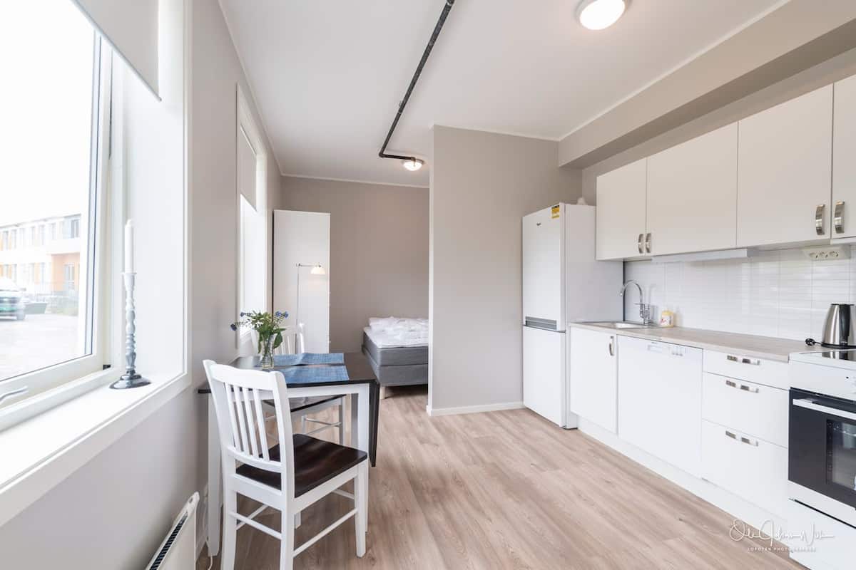 Een moderne keuken met witte kasten, een inbouwoven en een raam met uitzicht op de straat.