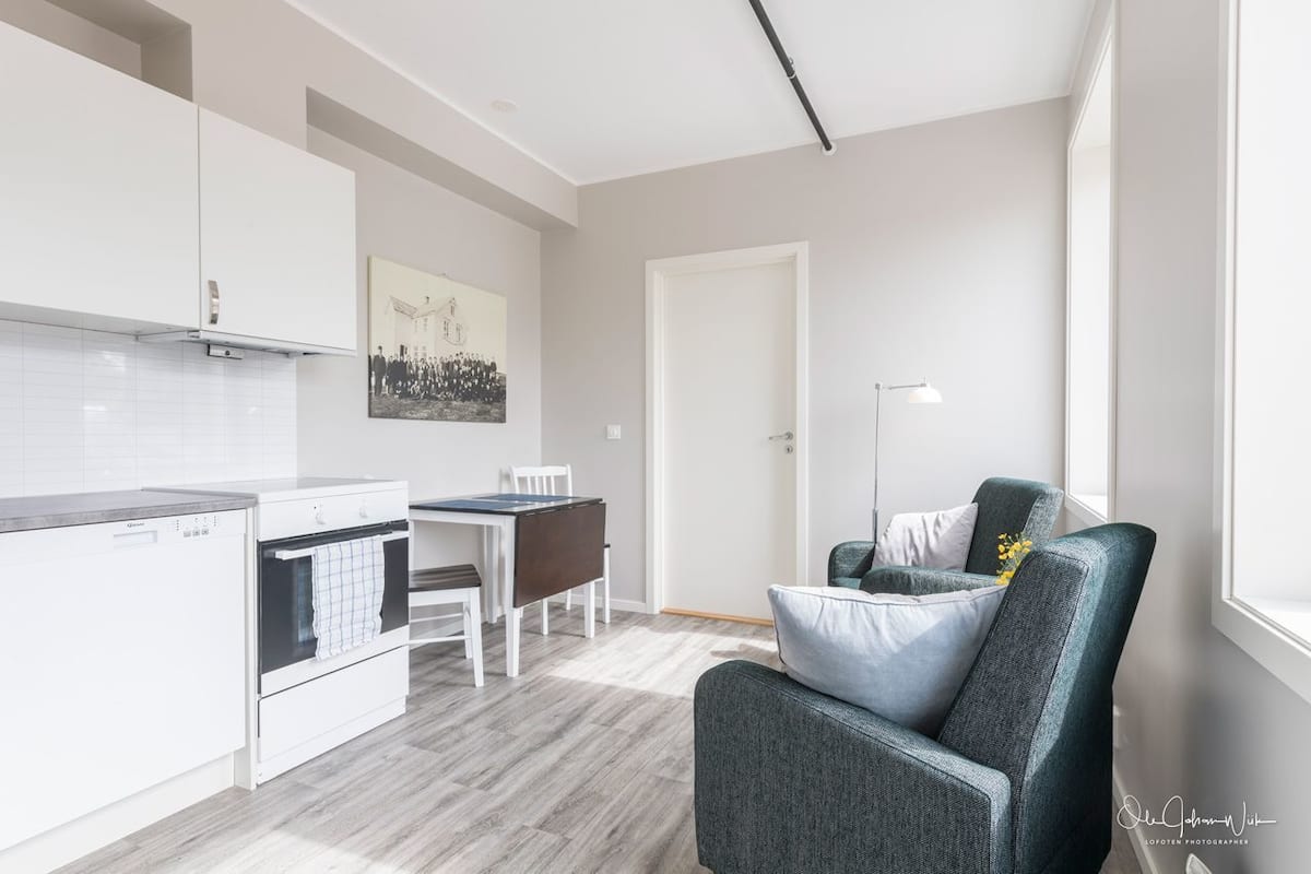Een moderne keuken met witte kasten, een eettafel met stoelen en een grijze fauteuil.