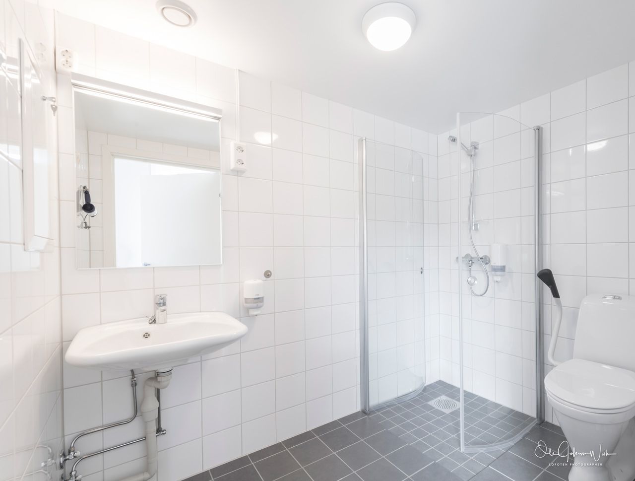 A modern bathroom with a white sink, mirror, and toilet, and a glass-enclosed shower area.