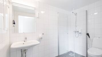 A modern bathroom with a white sink, mirror, and toilet, and a glass-enclosed shower area.