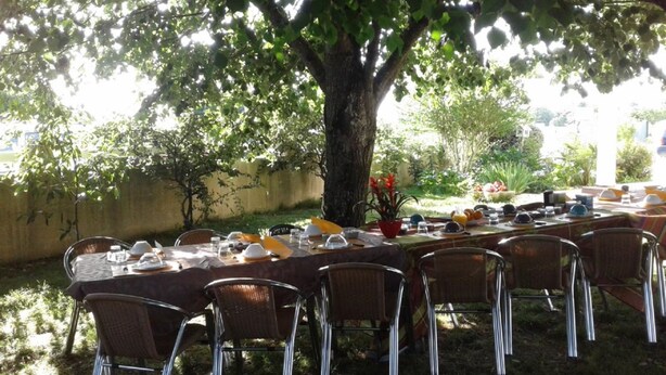 An outdoor dining area with a table set for a meal, surrounded by chairs, under a tree. - Maison Venitia Chambres d'hôtes (Aussonne)
