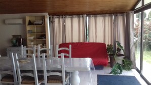 A living room with a dining table, chairs, a red sofa, a bookshelf, and a large window with curtains. - Maison Venitia Chambres d'hôtes (Aussonne)