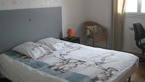 A bedroom with a bed, a nightstand, a chair, and a window with curtains. - Maison Venitia Chambres d'hôtes (Aussonne)