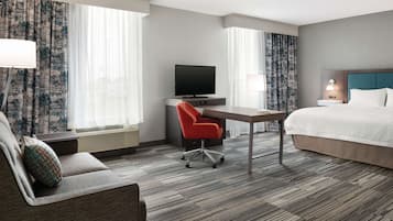 A hotel room with a bed, a desk with a TV, a red chair, and a sofa.