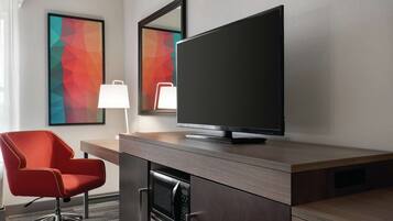 A modern hotel room with a flat-screen TV, a red office chair, a desk, and a microwave built into the cabinetry.