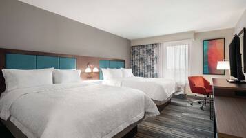 A hotel room with two beds, a desk with a chair, a TV, and a window with curtains.