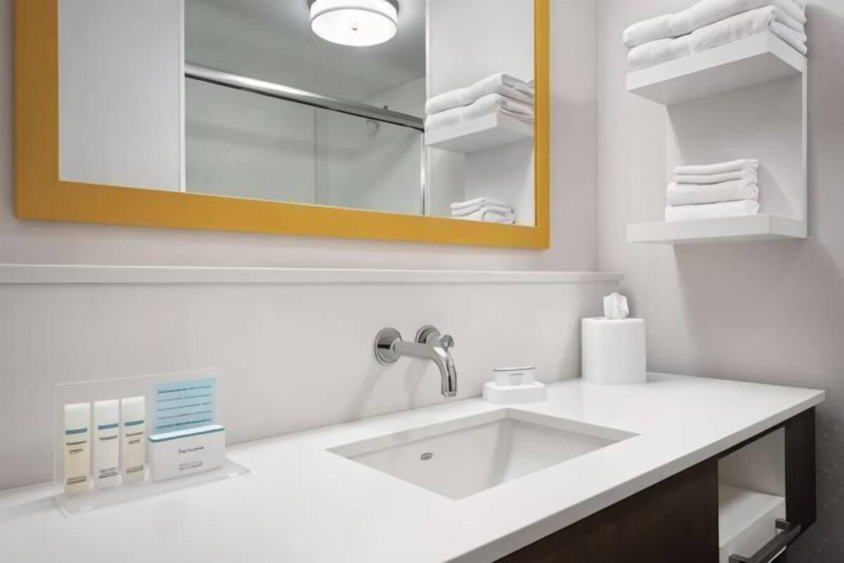 A hotel bathroom with a white sink, a mirror with a yellow frame, and a towel rack.