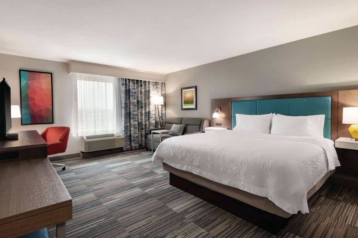 A hotel room with a large bed, a desk, a chair, a sofa, and a TV.