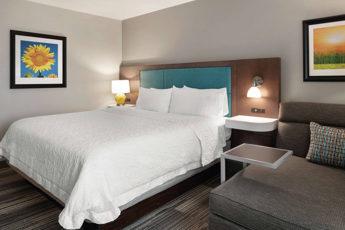 A hotel room with a large bed, a nightstand with a lamp, a small table, a sofa, and two wall-mounted lamps.