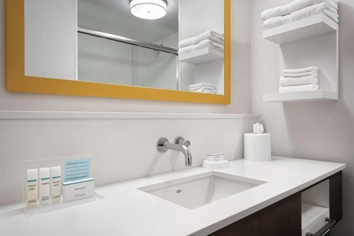 A hotel bathroom with a white sink, a mirror with a yellow frame, and a towel rack.