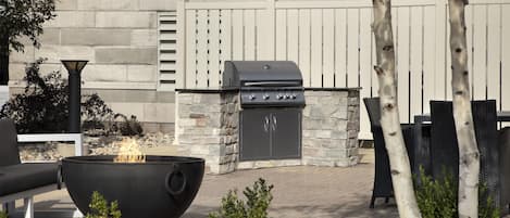 An outdoor patio with a stone barbecue grill, a fire pit, and outdoor seating.