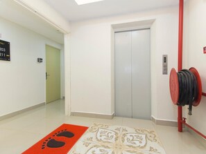Un pasillo con una puerta, un carretel de manguera contra incendios y un felpudo con diseño de huella de pata.