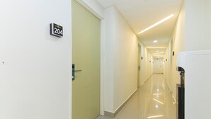 Um corredor longo e bem iluminado, com uma porta identificada com o número '204' e um bebedouro à direita.