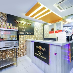 A hotel reception desk with a sign reading 'HOTEL KL CENTRE POINT,' a refrigerator with beverages, and a digital display. - Hotel KL Centre Point (Kuala Lumpur)