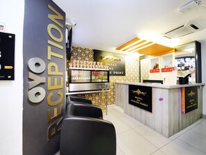 Zona de recepción de un hotel con mostrador, área de asientos y refrigerador de pared.