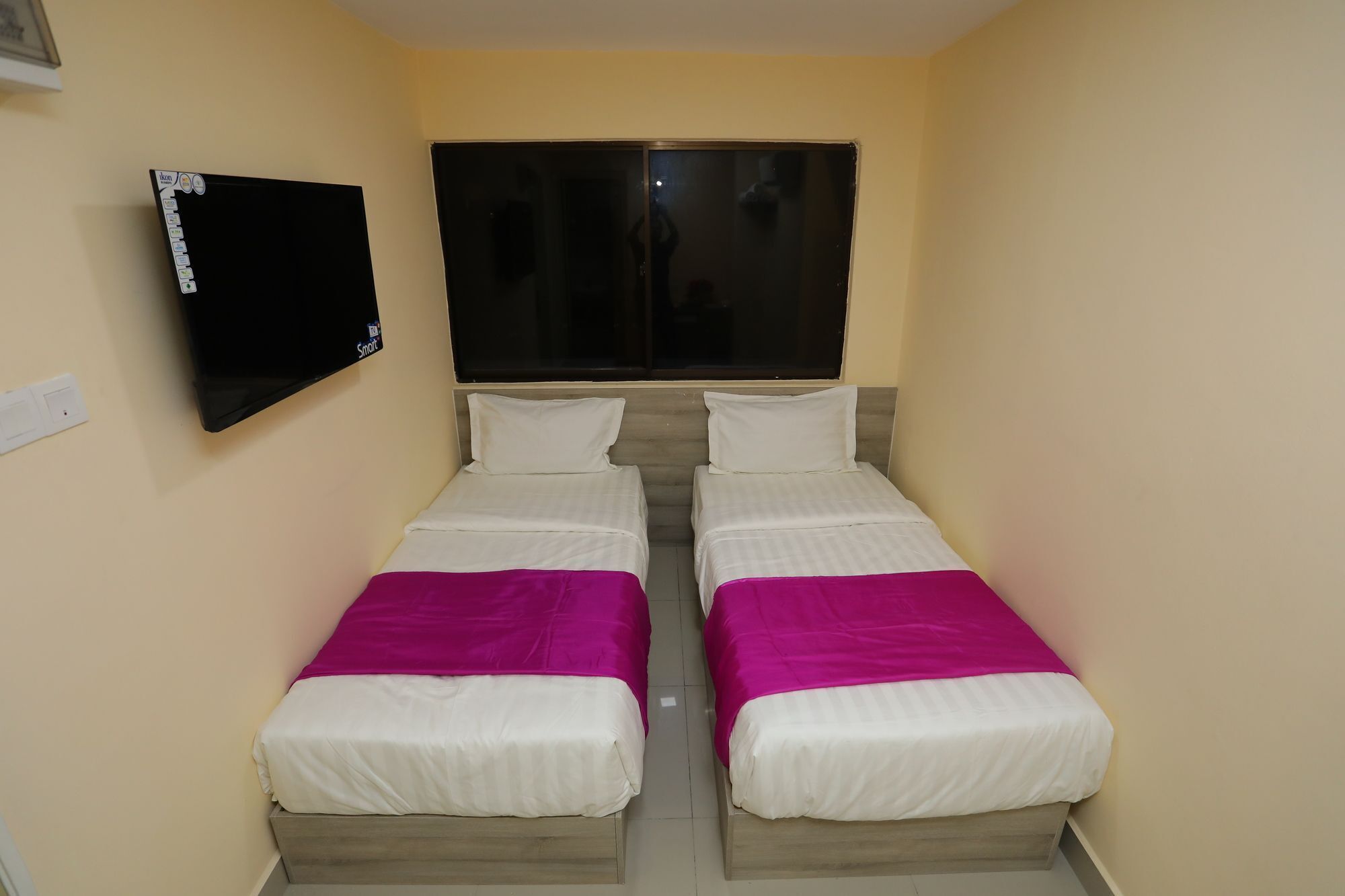 Une petite chambre avec deux lits, un téléviseur à écran plat fixé au mur et une fenêtre située au-dessus des lits.