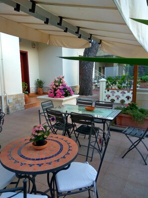 Eine Terrasse im Freien mit einem runden Tisch und Stühlen, einem Grill und Topfpflanzen.