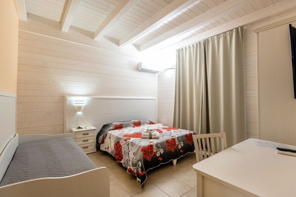 A bedroom with a bed, bedside table, lamp, and a small desk with a chair.