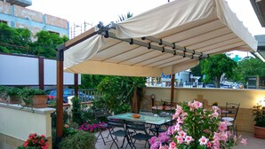 An outdoor patio with a covered table and chairs, surrounded by potted plants and flowers. - Le Camelie (Ginosa)