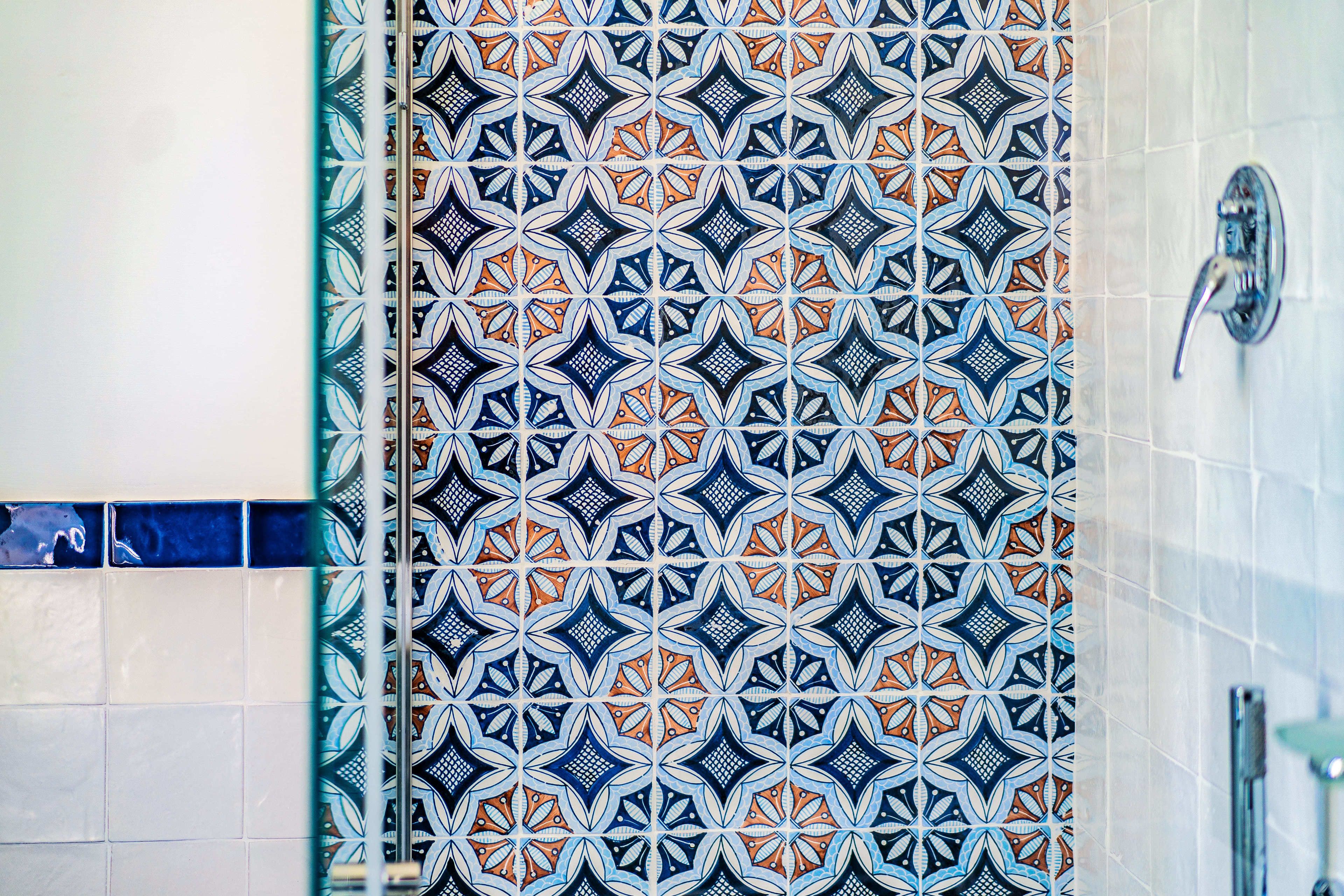 A bathroom with a patterned tile backsplash and a shower area.