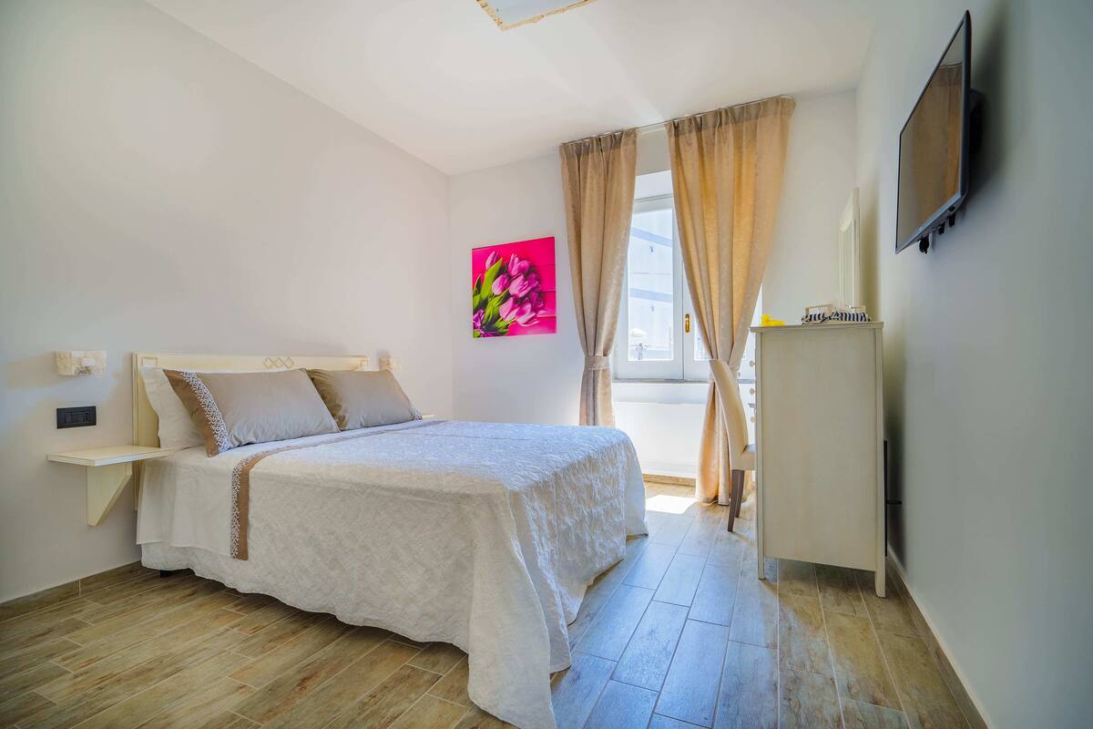 Ein Schlafzimmer mit einem Bett, einem Nachttisch, einem Fernseher und einem Fenster mit Vorhängen.
