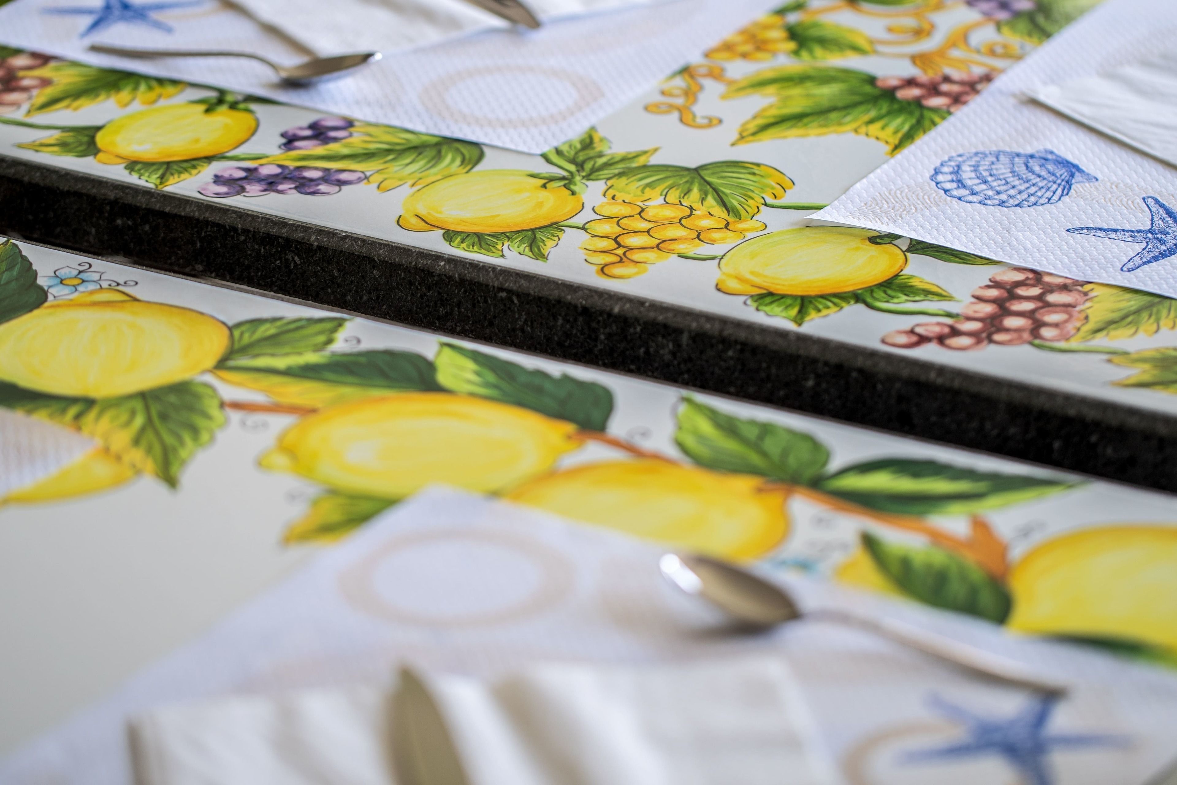 Un comptoir de cuisine avec un pare-feu décoré de motifs de fruits, une cuillère et une serviette.