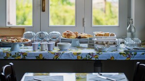 A breakfast buffet with various pastries and beverages, set against a backdrop of large windows with a view of greenery. - Lemon Factor Sorrento (Sorrento)
