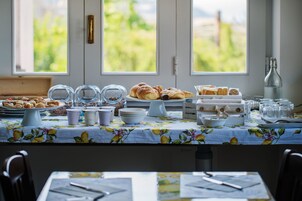 Un bufé de desayuno con diversos pasteles y bebidas, con vistas a la naturaleza a través de amplias ventanas.