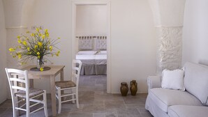 A room with a dining table, two chairs, a sofa, and a bed with a white headboard. There are two vases on the floor near the sofa. - Masseria Capece (Cisternino)