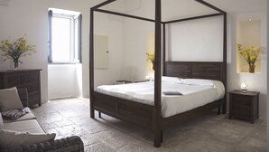 A four-poster bed in a bedroom with a white headboard, a bedside table with a lamp, and a window with curtains. - Masseria Capece (Cisternino)
