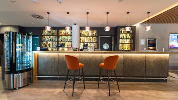 Eine Bar mit einer Theke, zwei orangefarbenen Barhocker und einem großen Kühlschrank.