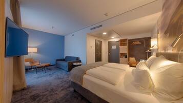 A hotel room with a large bed, a desk, a chair, a sofa, a television, and a wall-mounted light fixture.