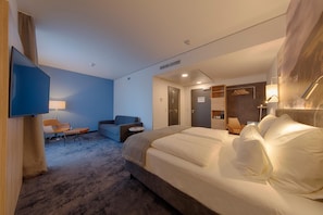 Habitació d'hotel amb un llit gran, escriptori, cadira, sofà, televisió i llum penjada a la paret.