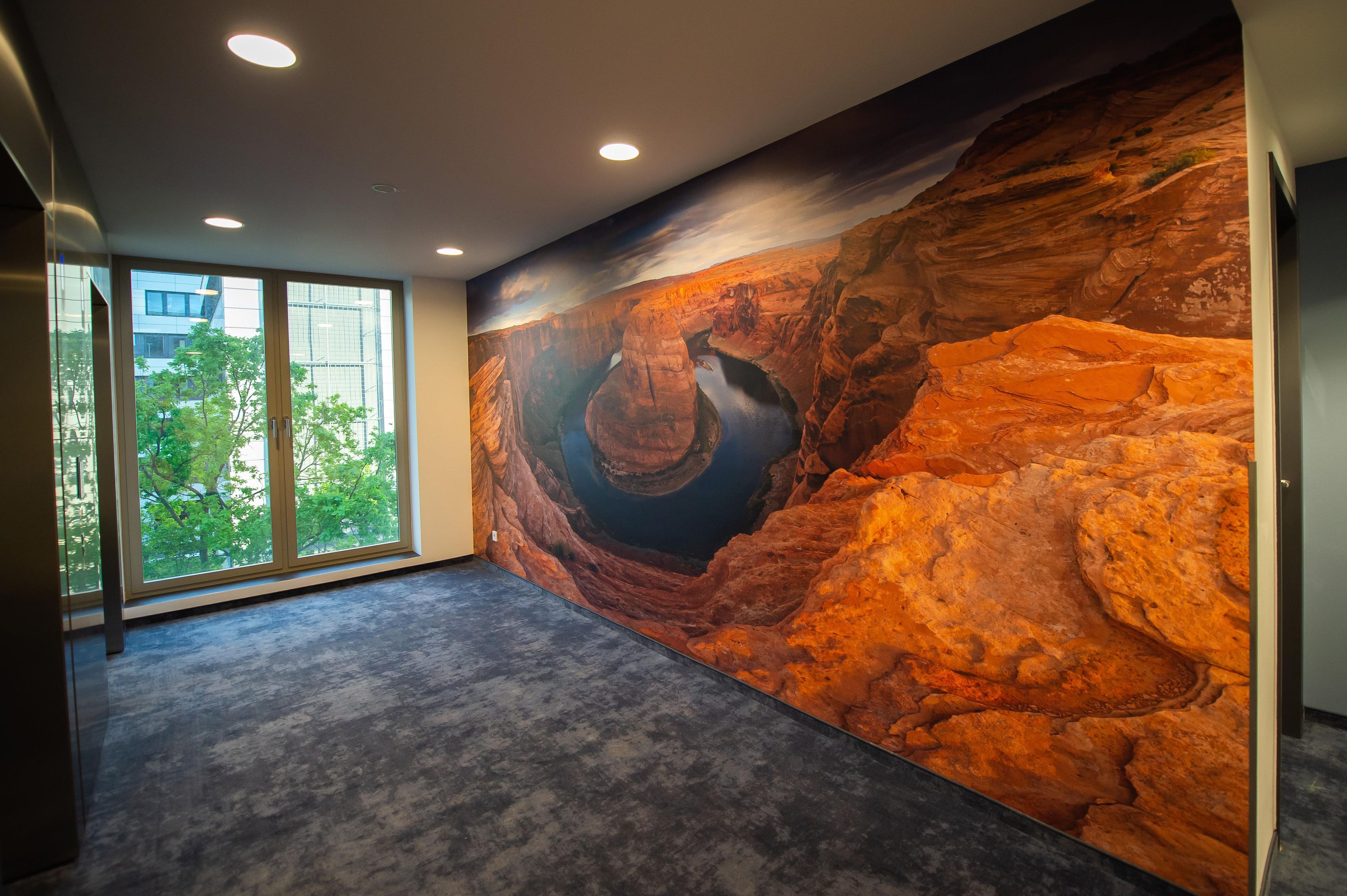 A room with a large window, a mural of a canyon, and a modern interior design.