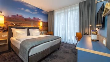 Quarto de hotel com uma cama grande, uma escrivaninha, uma cadeira, uma televisão e um mural com paisagem desértica.