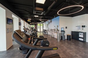 Un gimnasio con cintas de correr, bicicletas estáticas y un dispensador de agua.