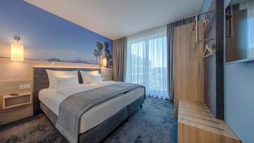 Ein Hotelzimmer mit einem großen Bett, einem Holfnachtkästchen, einem an der Wand befestigten Fernseher und Blick auf den Strand.