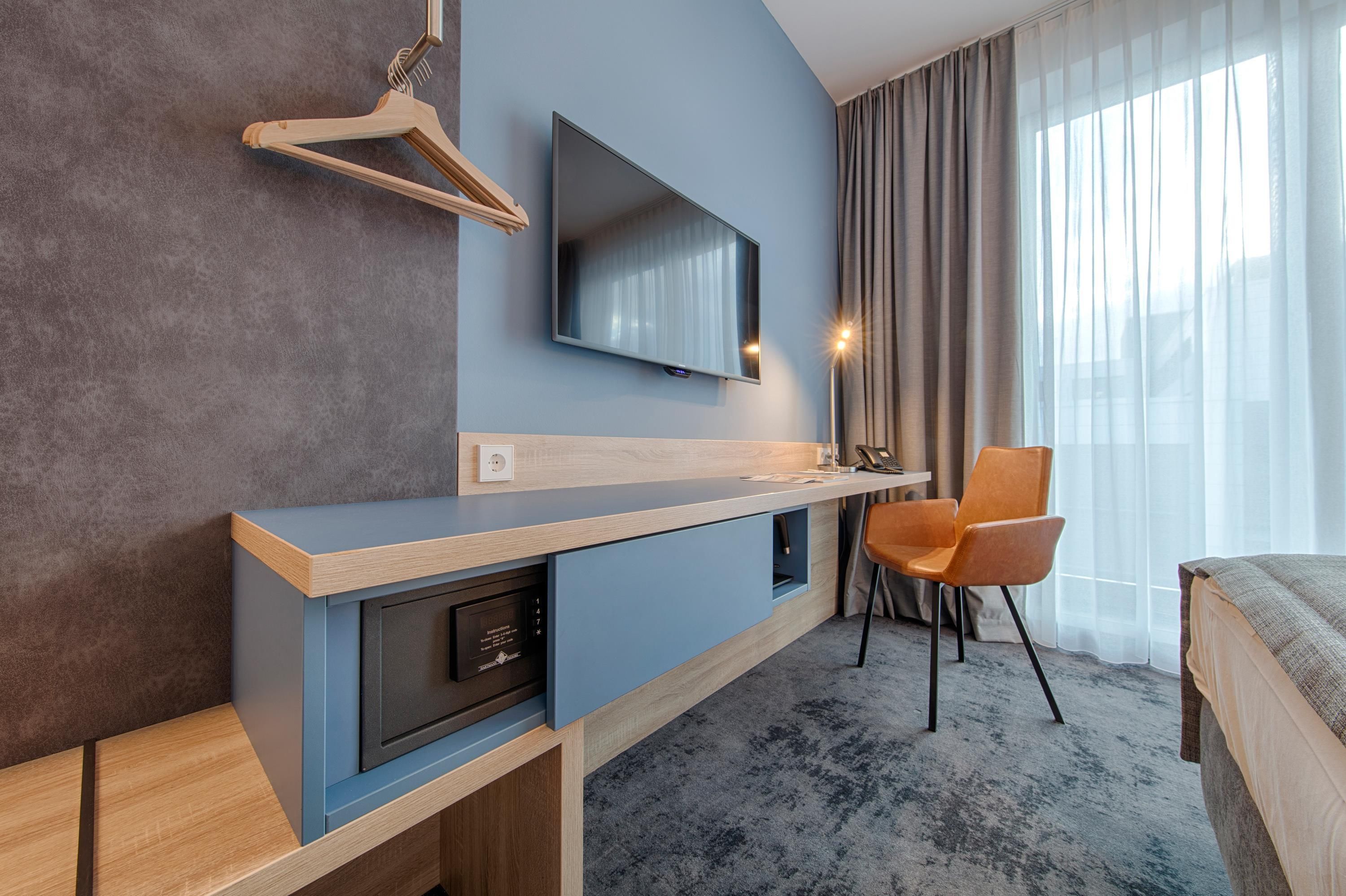 Una habitación de hotel moderna con escritorio integrado, televisor de pantalla plana en la pared, una silla y una cama.