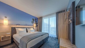 Una habitación de hotel moderna con una cama grande, una mesita de noche de madera, televisión integrada y vista al mar.