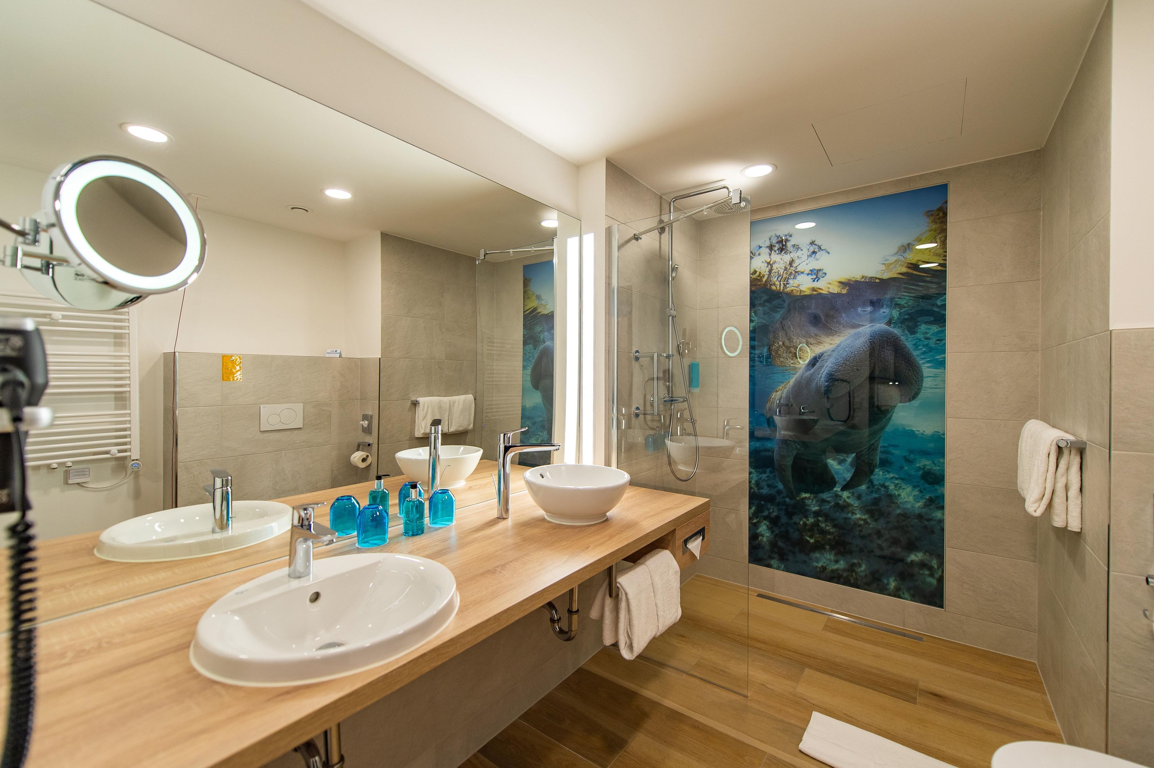 A modern bathroom with two sinks, a large mirror, a glass shower enclosure, and a wall mural of a sea creature.