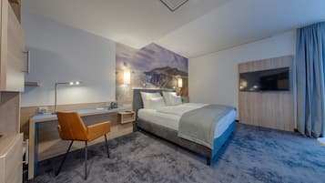 A hotel room with a bed, desk, chair, and a TV.