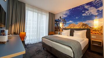 Ein Hotelzimmer mit einem Bett, einem Schreibtisch, einem Sessel, einem Nachttisch und einem großen Fenster mit Vorhängen.