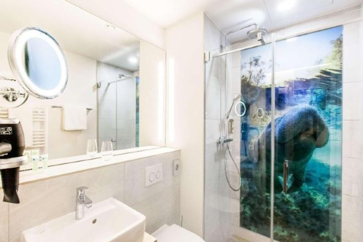 Un baño con lavamanos, espejo y cabina de ducha con un paisaje submarino.