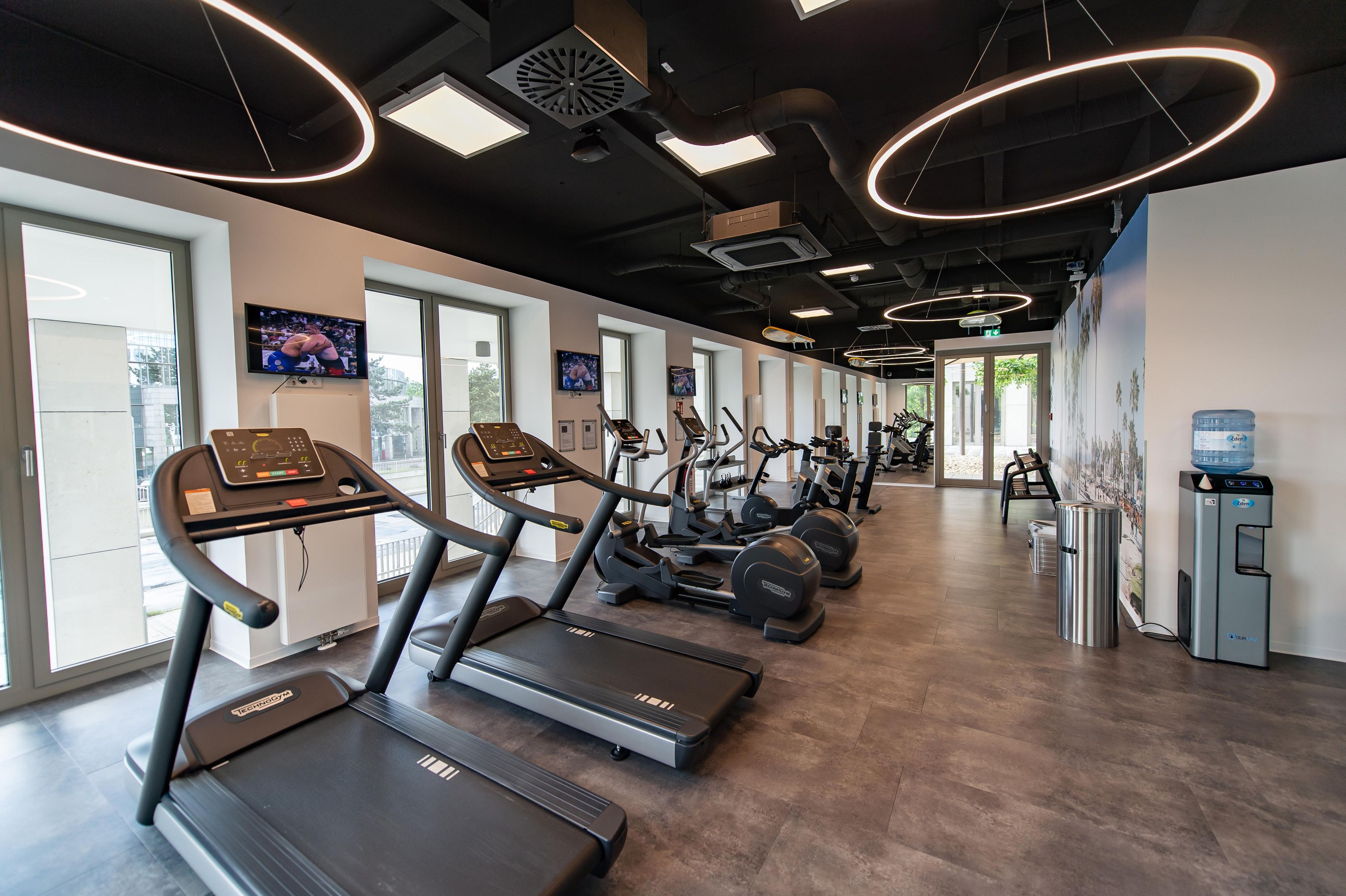 Un gimnasio con cintas de correr, bicicletas estáticas y un dispensador de agua.