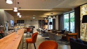 Zona de bar moderna con mostrador de madera, sillas naranjas y un área de descanso con sofás y sillones.