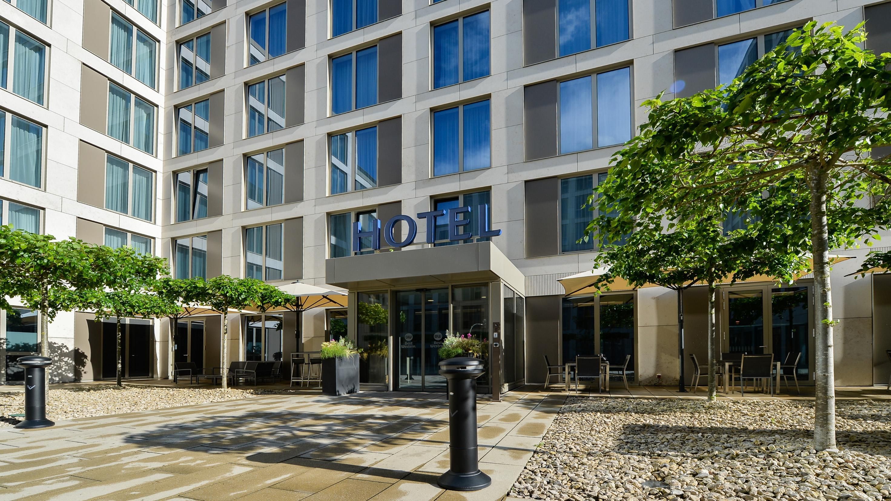 A hotel with a modern facade, large windows, outdoor seating, and a sign indicating it is a Best Western hotel.